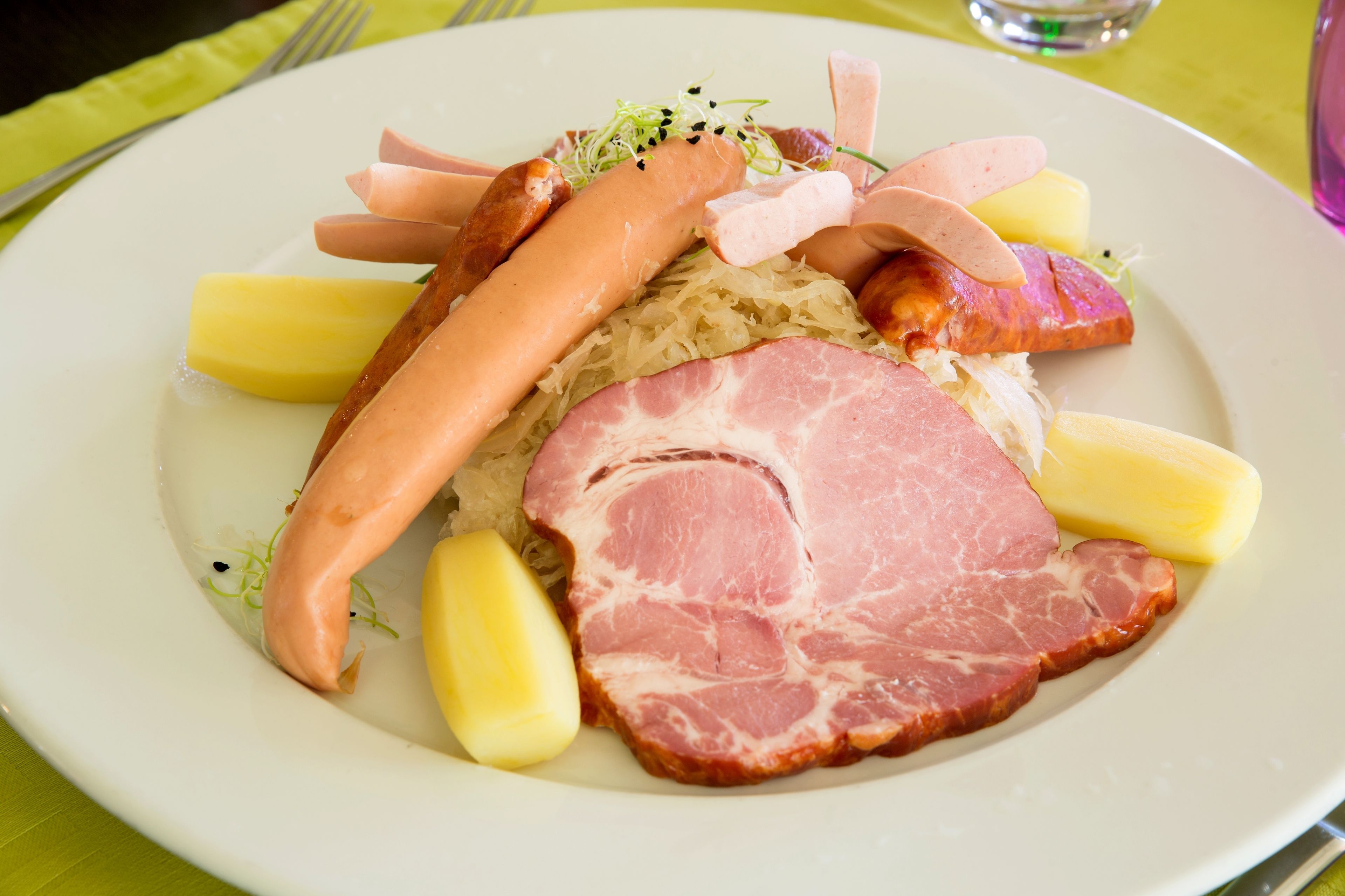 A plate of food with sausages, ham, and potatoes.