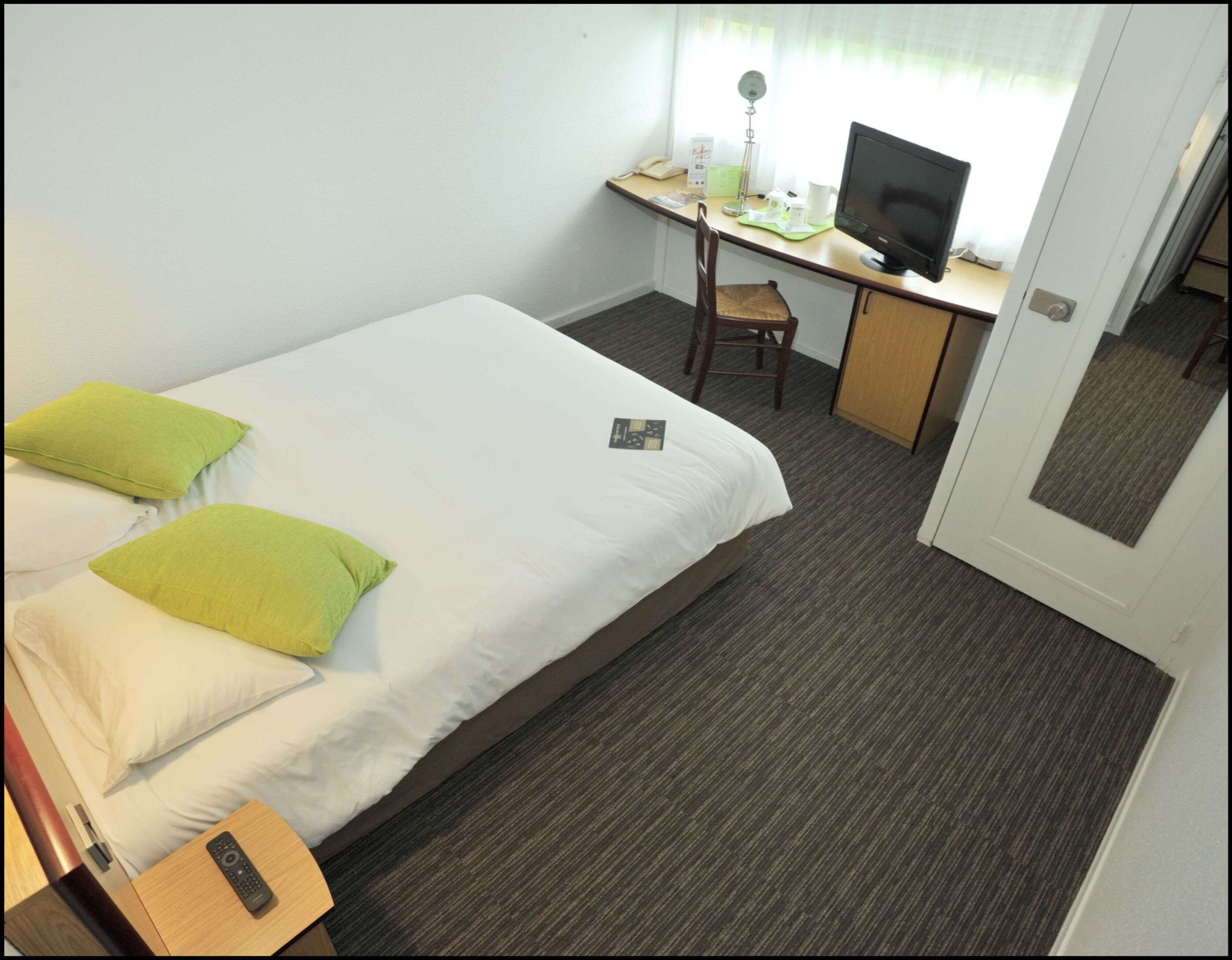 Una habitación de hotel con una cama, un escritorio con una computadora y una silla.