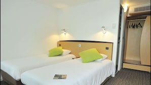 Een hotelkamer met twee enkele bedden, elk voorzien van een kussen en een bedlampje. Er is een houten garderobe met kledingroede en een deur.