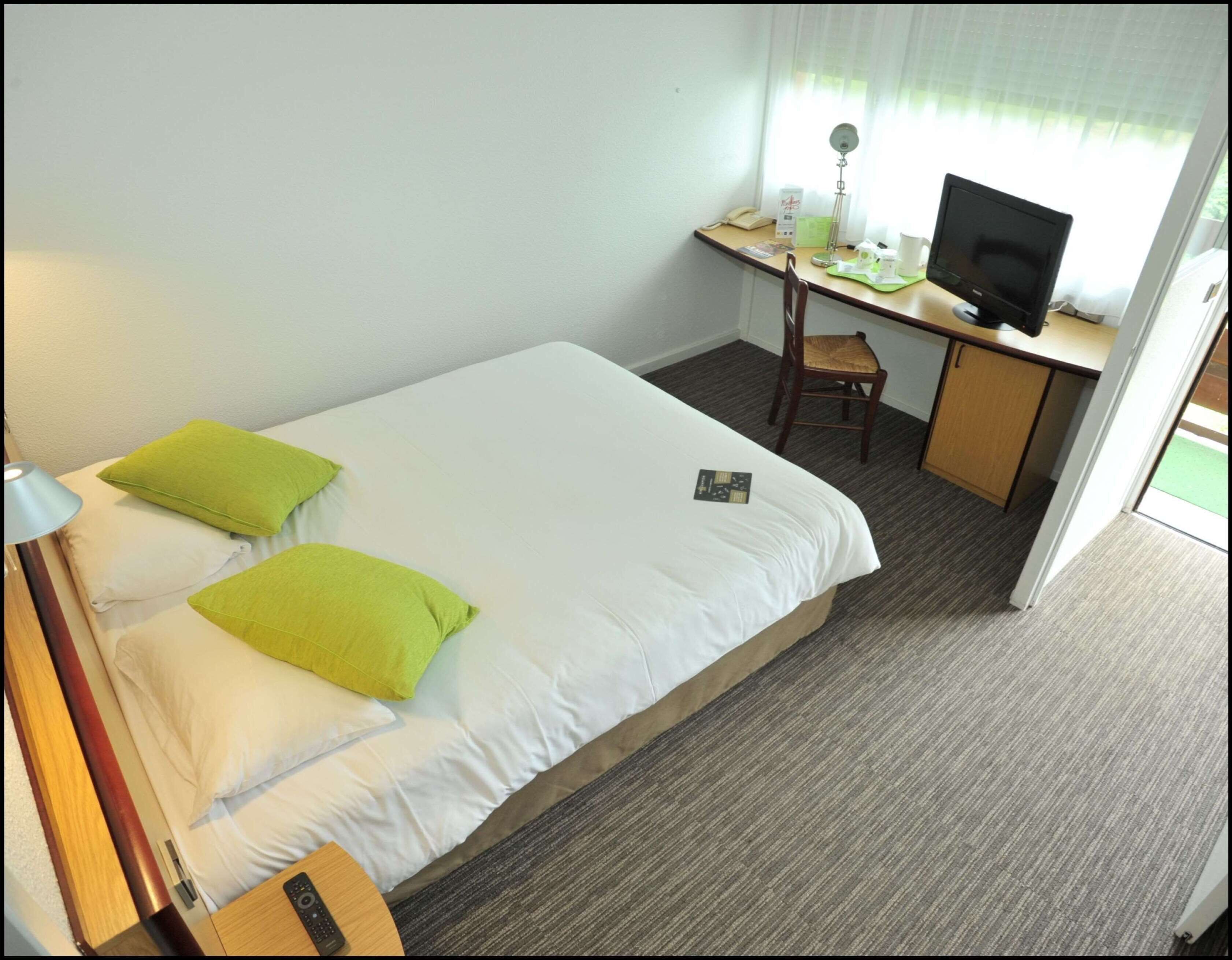 A hotel room with a bed, a desk, a chair, a television, and a lamp.