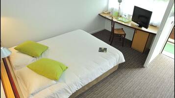 Ett hotellrum med en säng, ett skrivbord, en stol, en tv och en lampa.