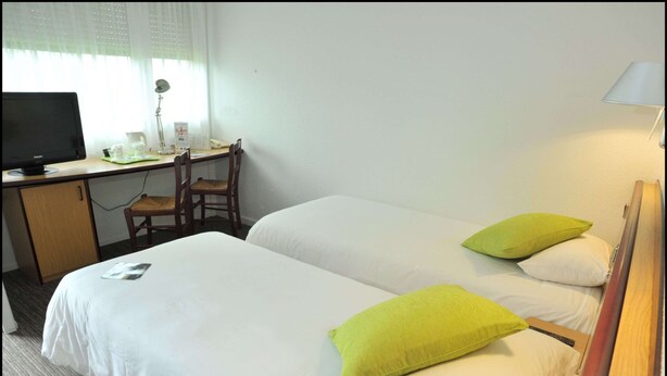 Een hotelkamer met twee bedden, een bureau met een computer, een stoel en een lamp.