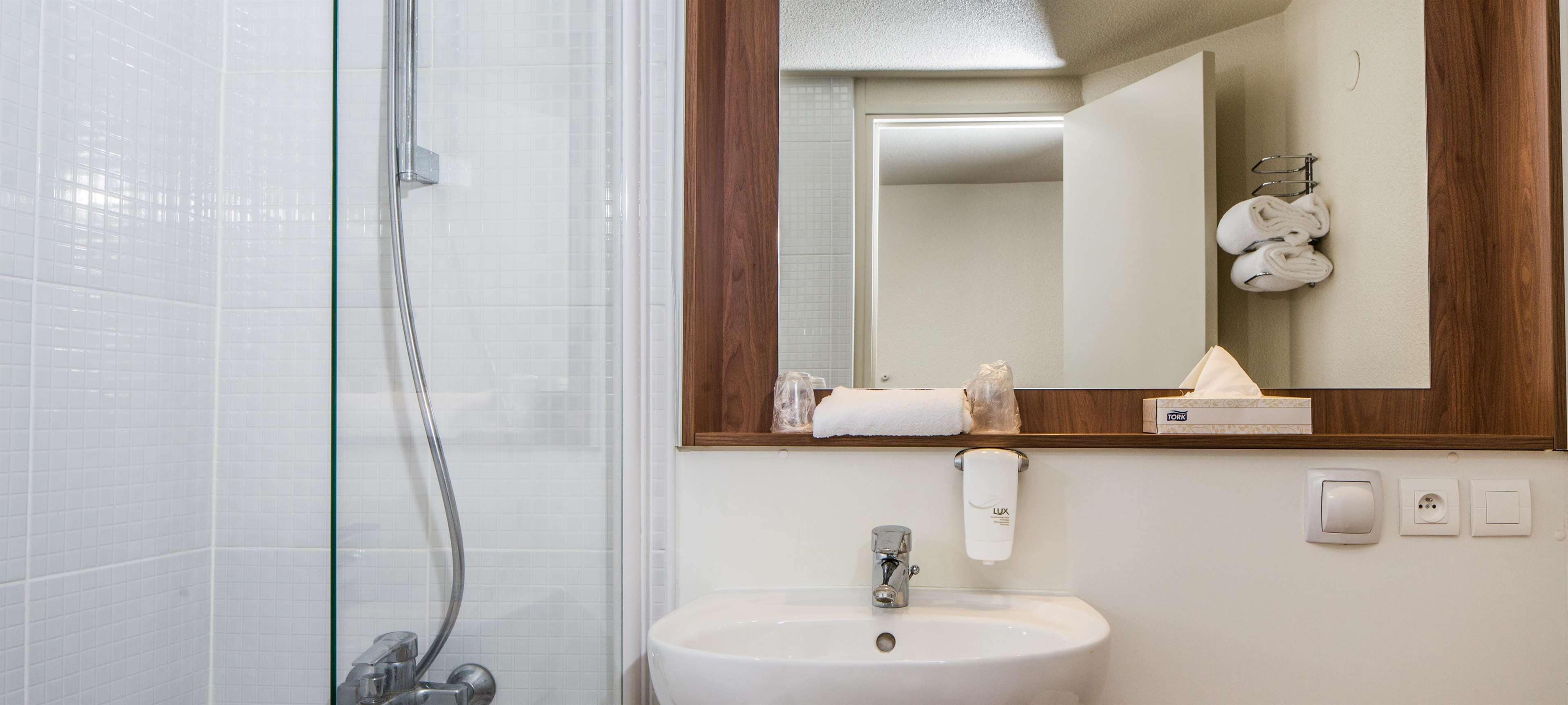 A bathroom with a glass shower enclosure, a sink with a mirror above it, and a towel rack with towels.