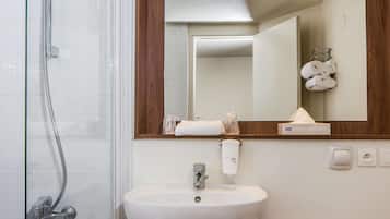 Un baño con cabina de ducha de vidrio, un lavabo con espejo y un perchero con toallas.