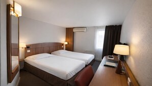 A hotel room with two beds, a desk, a chair, a mirror, and a window with curtains.