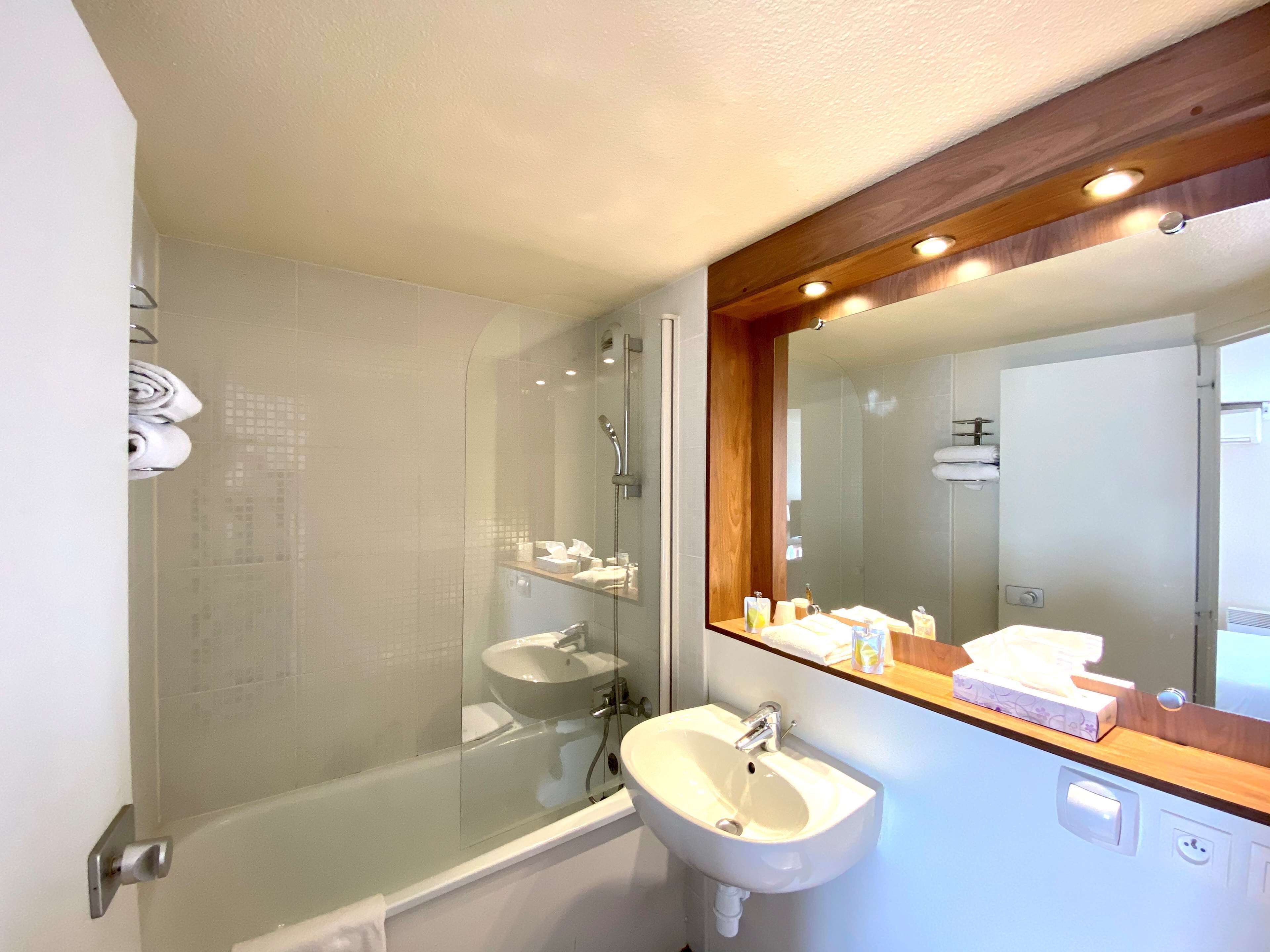 A bathroom with a glass-enclosed shower, a sink, and a mirror with a wooden frame.