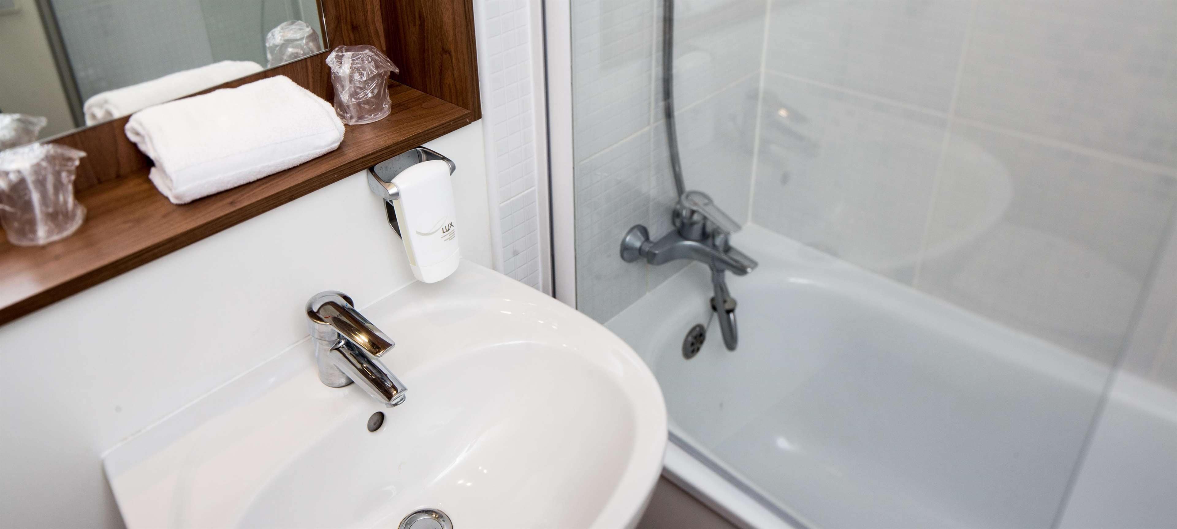 Un baño con lavamanos blanco, espejo, toallero y zona de ducha.