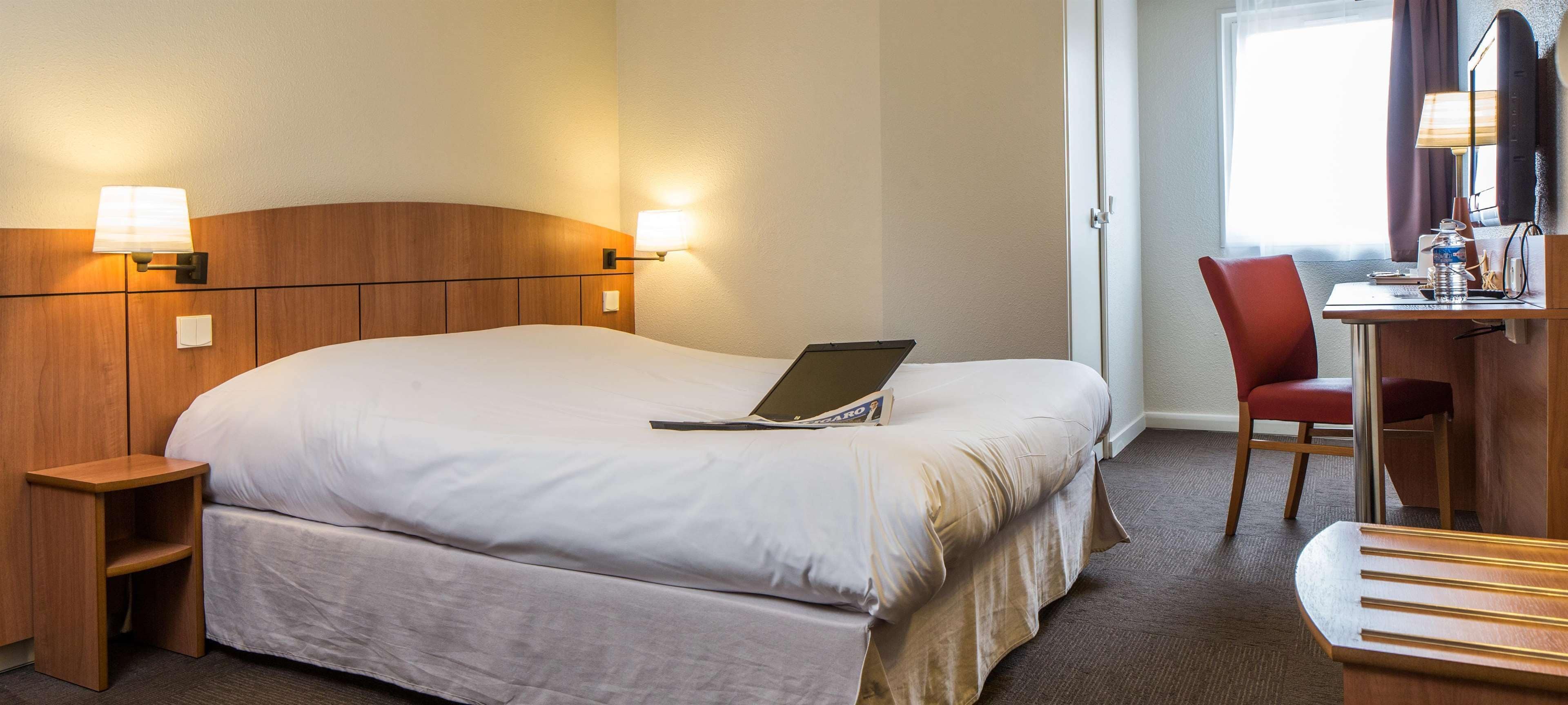 Una habitación de hotel con una cama grande, un escritorio con una silla, una computadora portátil y un televisor.