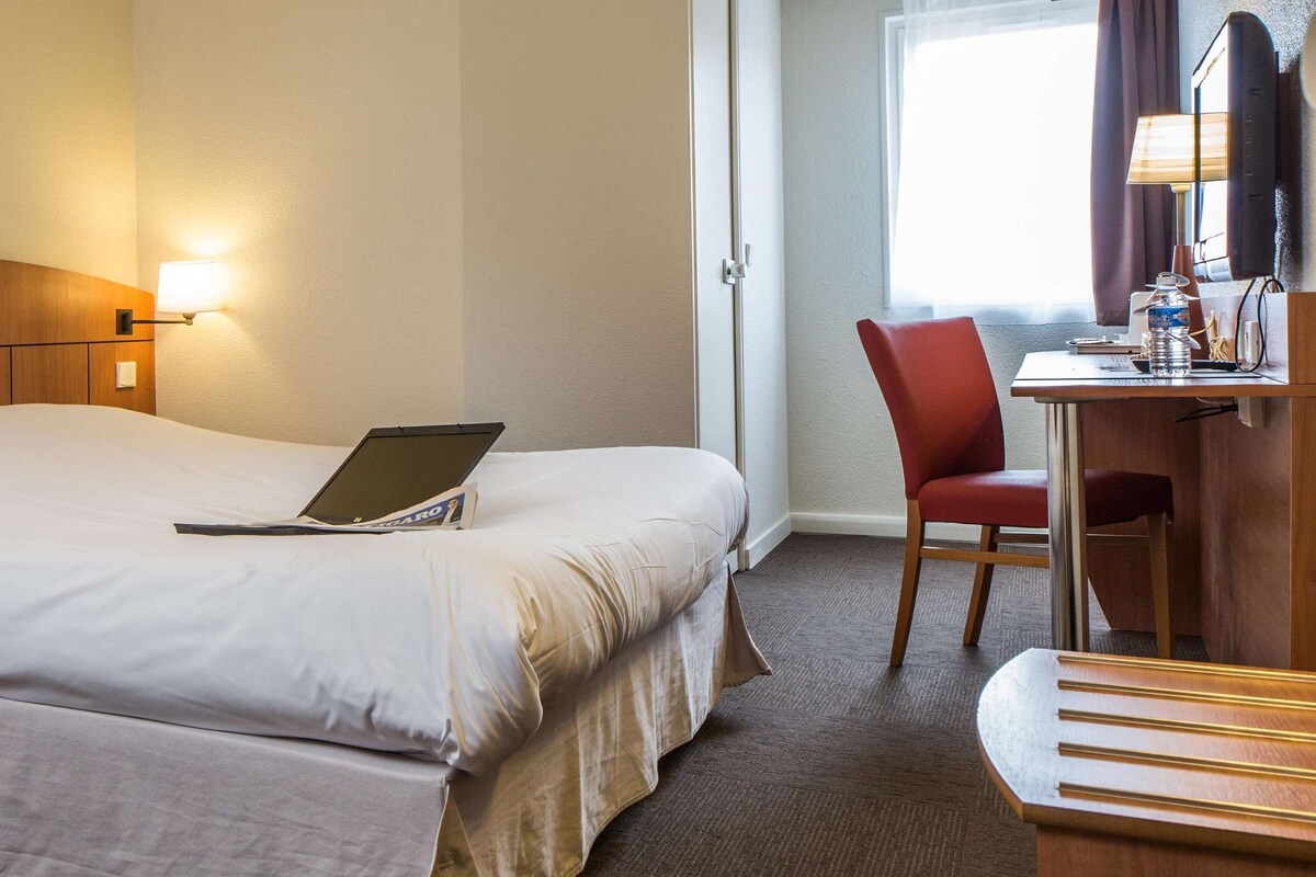 A hotel room with a large bed, a desk with a chair, a laptop, and a TV.