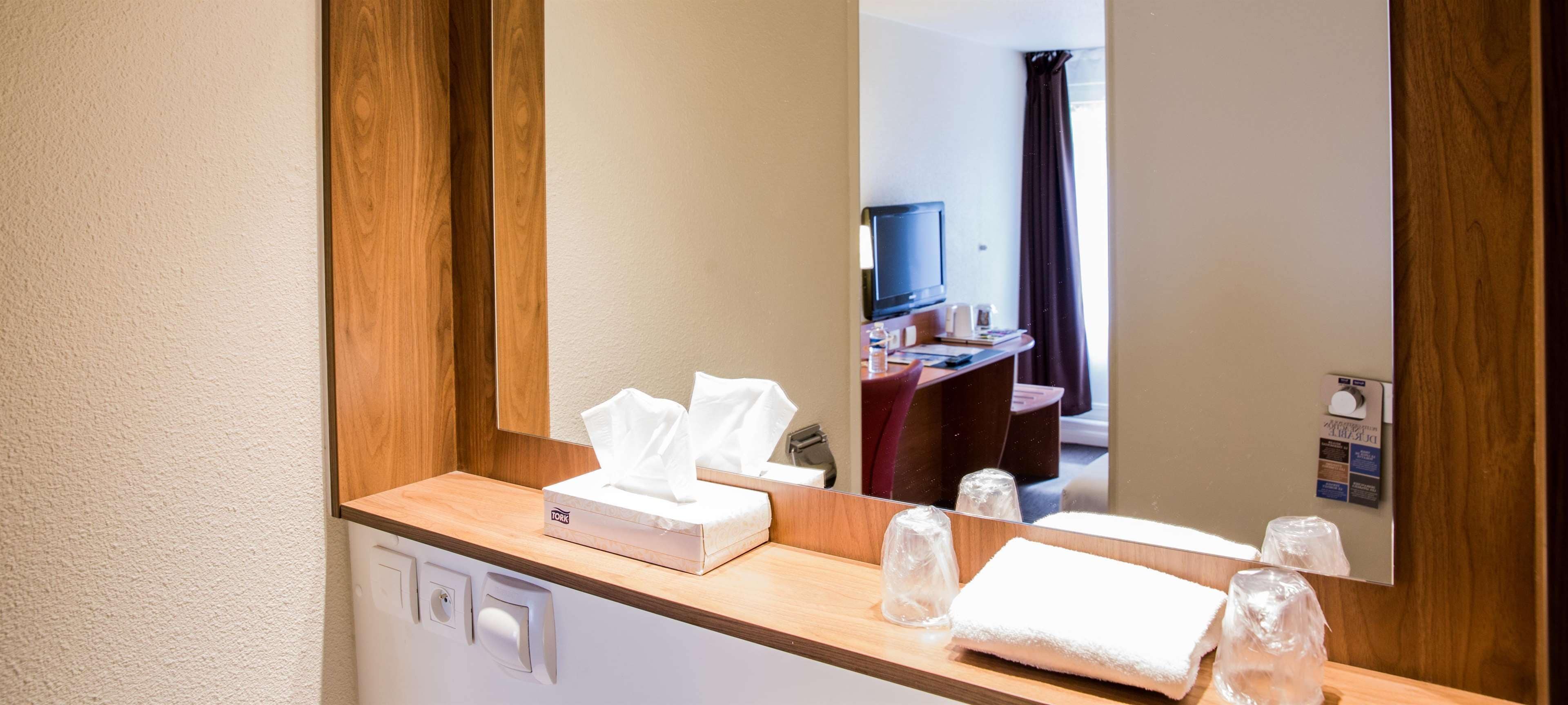 Un baño de hotel con un tocador de madera, un espejo, una caja de pañuelos y una toalla.