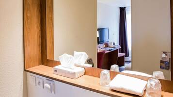 Un baño de hotel con un tocador de madera, un espejo, una caja de pañuelos y una toalla.