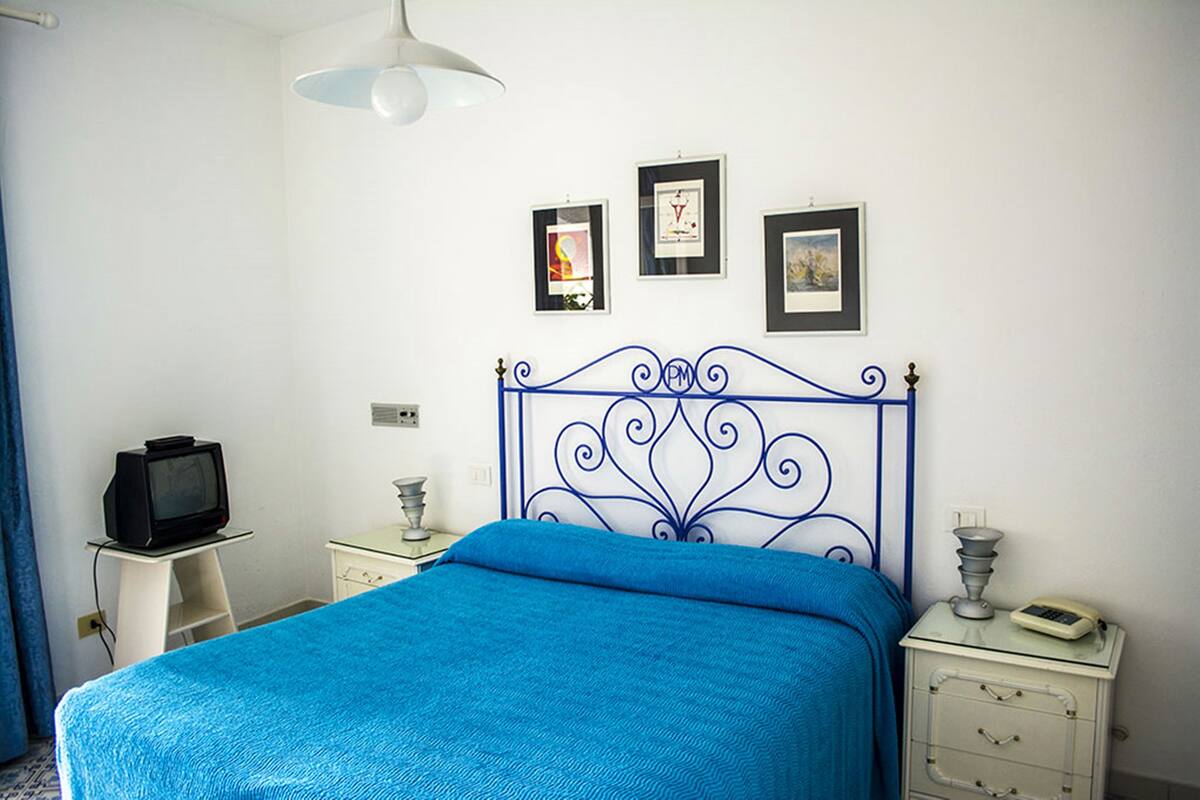 Une chambre avec une couvre-lit bleue, un téléviseur posé sur une petite table et des tableaux encadrés accrochés au mur.