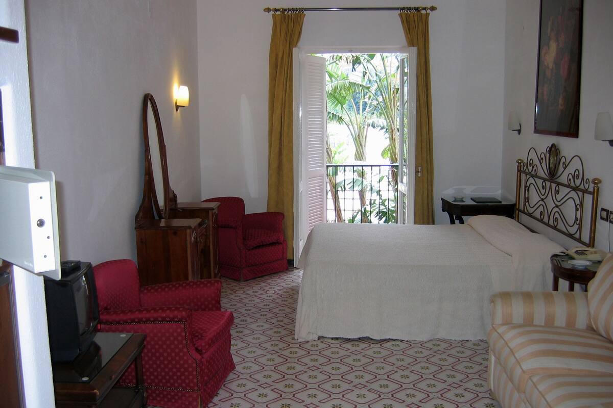 Une chambre d’hôtel comprenant un lit, un bureau avec un ordinateur, une chaise, une commode et un miroir.
