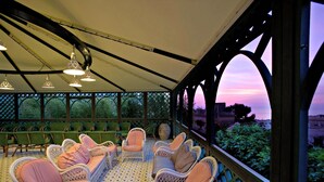 Un área de estar al aire libre con techo, con sillas de mimbre y un piso estampado, con vistas a un jardín y al atardecer.
