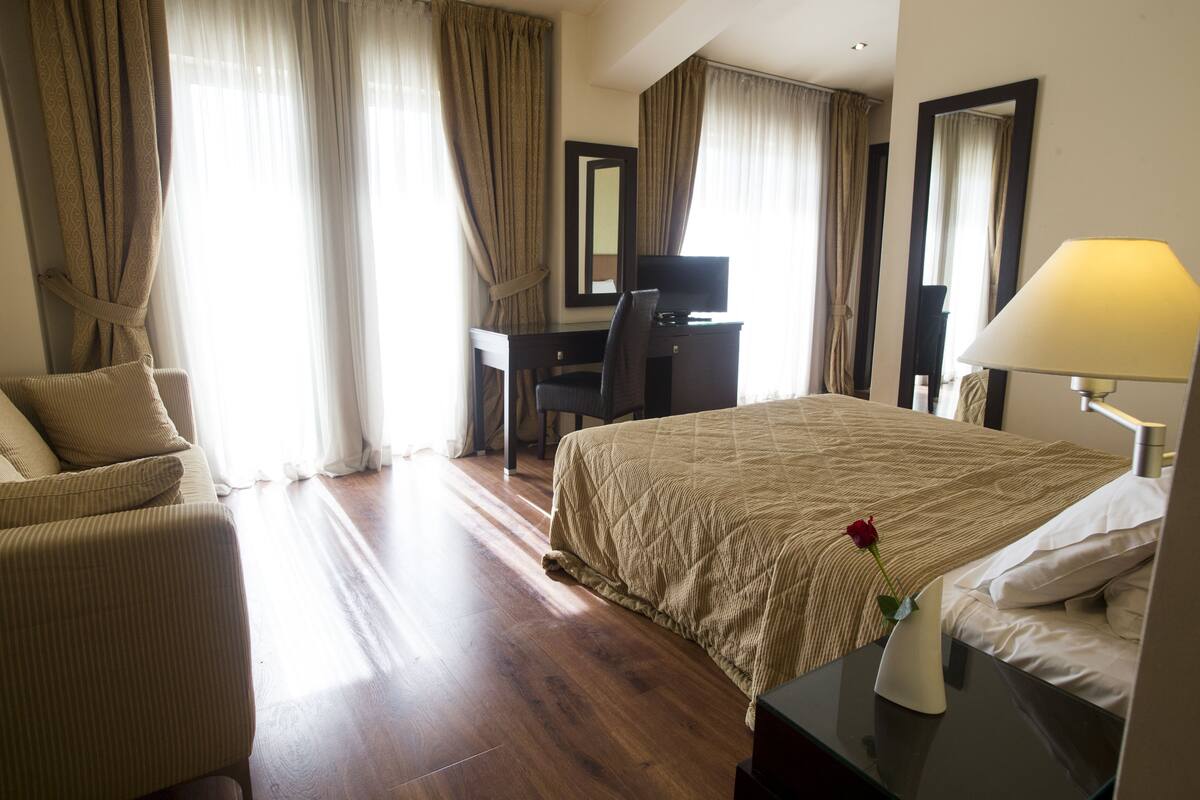 Een hotelkamer met een bed, een bureau, een stoel, een lamp en een vaas met een bloem.