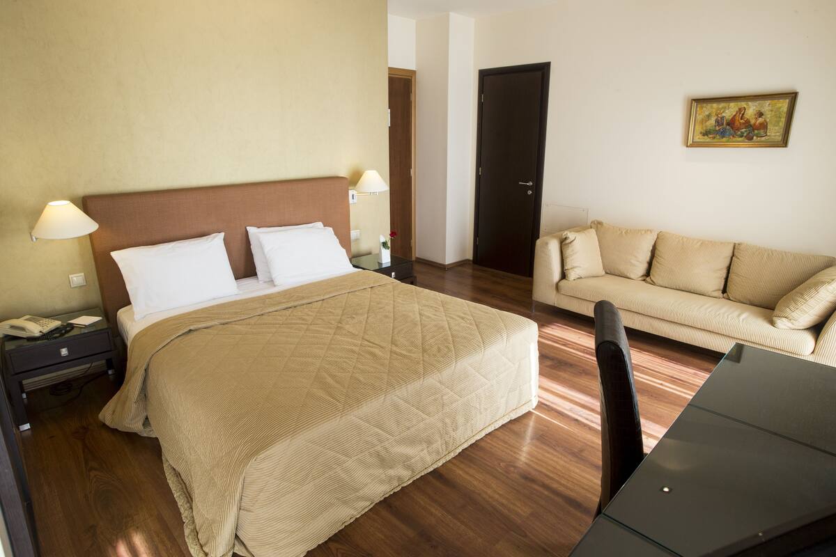 Een hotelkamer met een bed, nachtkastje, lamp en een bank.