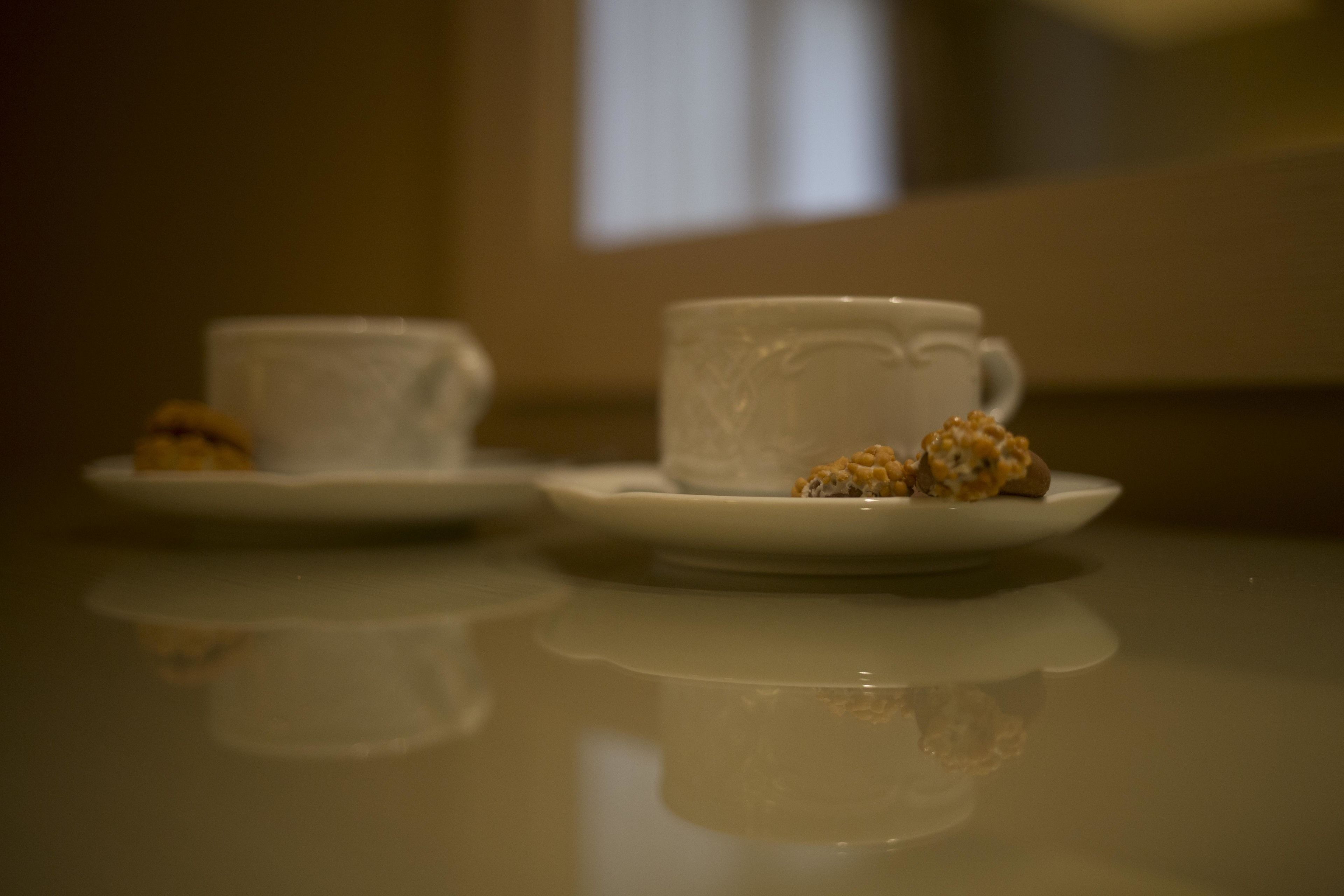 A table with two white cups and saucers, each with a small pastry.