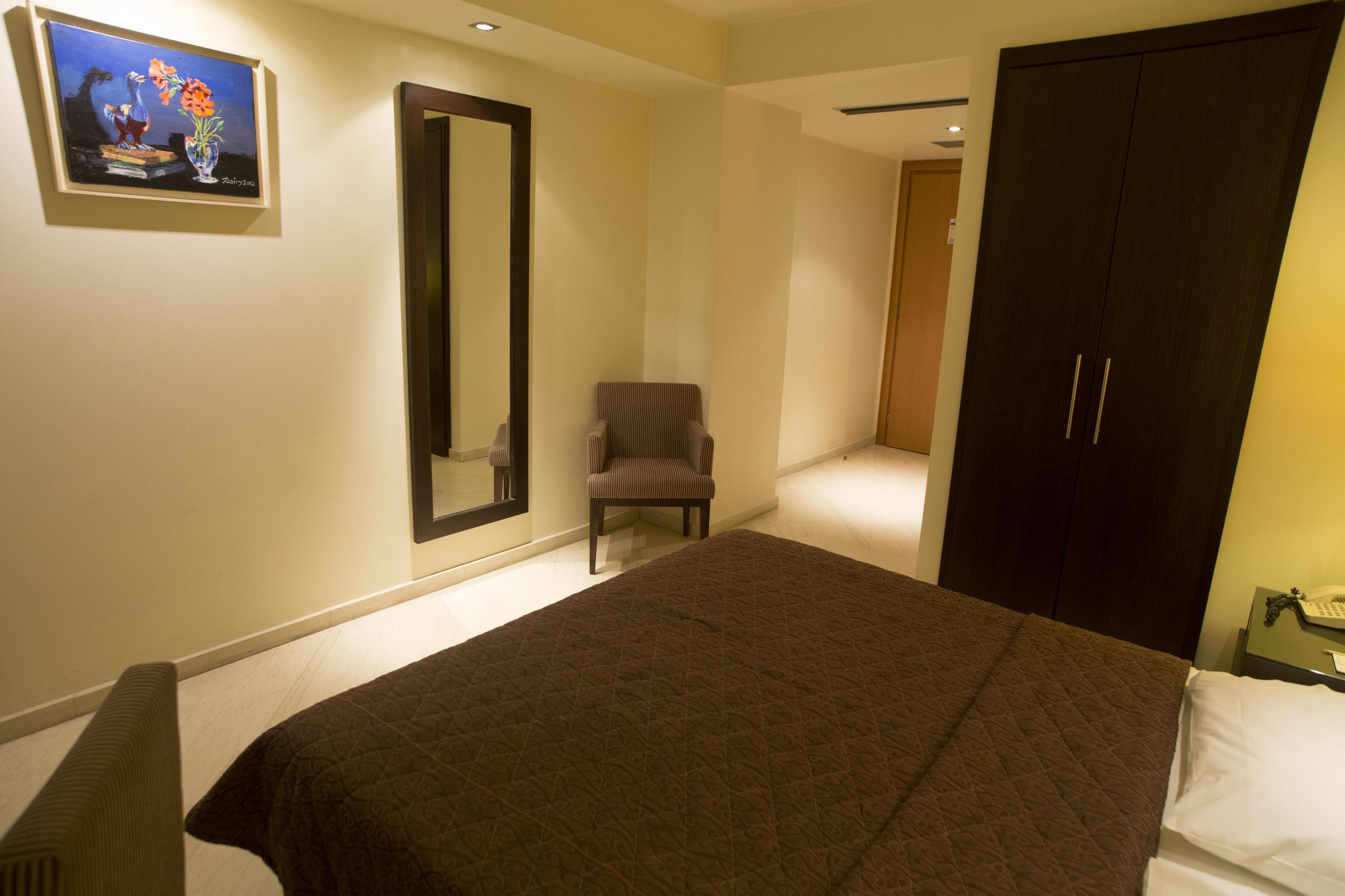 A bedroom with a large bed, a chair, a wardrobe, and a painting on the wall.