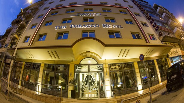 L’hôtel Tobacco se distingue par son entrée imposante, ses nombreuses fenêtres et un panneau indiquant un espace de stationnement.