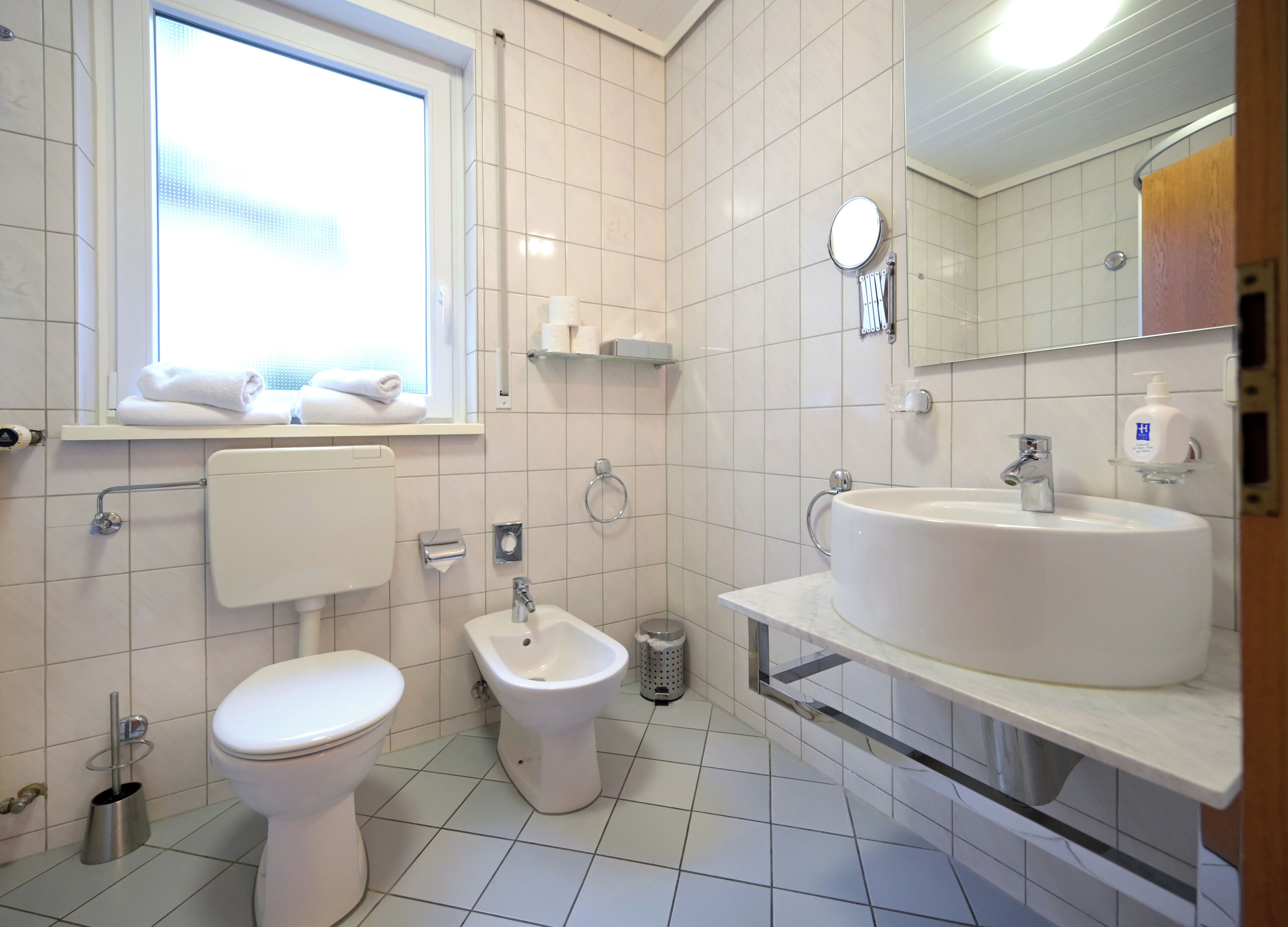 A modern bathroom with a toilet, bidet, and a large sink with a mirror above it.