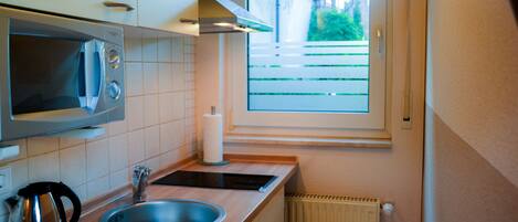Cocina compacta con microondas, lavamanos, hervidor y ventana con vista a una cerca y vegetación.