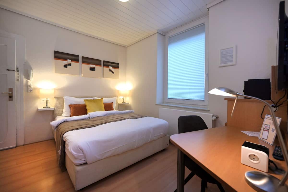 Une chambre à coucher avec un lit, des lampes de chevet, un bureau avec une lampe, une chaise et une fenêtre avec des stores.