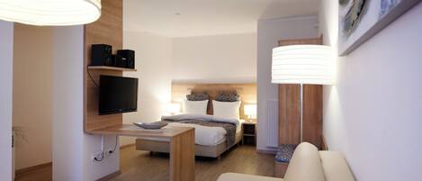 Ein modernes Hotelzimmer mit Bett, Nachttischen, Fernseher und einer Couch.