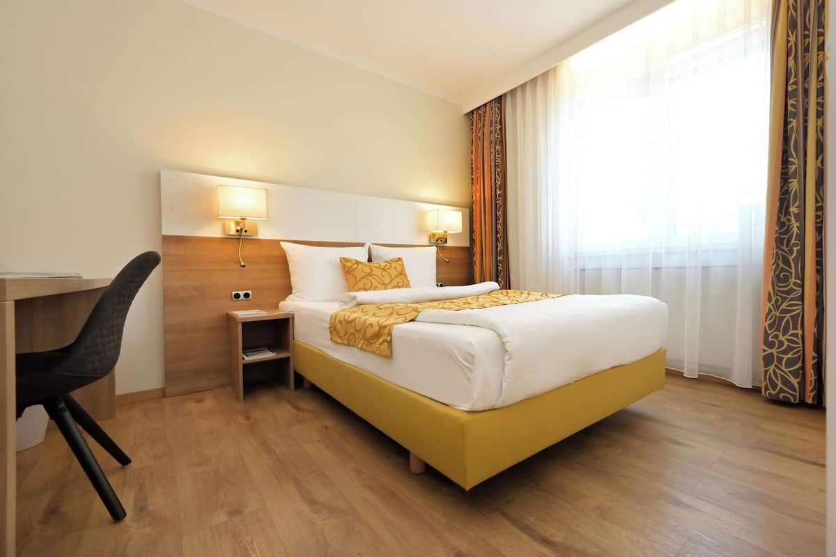 Une chambre d’hôtel comprenant un lit, un bureau, une chaise, des tables de chevet et des rideaux.