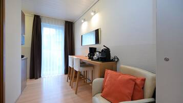 A hotel room with a sofa, a desk with a coffee maker, and a chair.