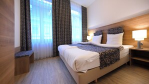 Ein Hotelzimmer mit einem großen Bett, einem Nachttisch mit Lampe und einem Fenster mit gemusterten Vorhängen.