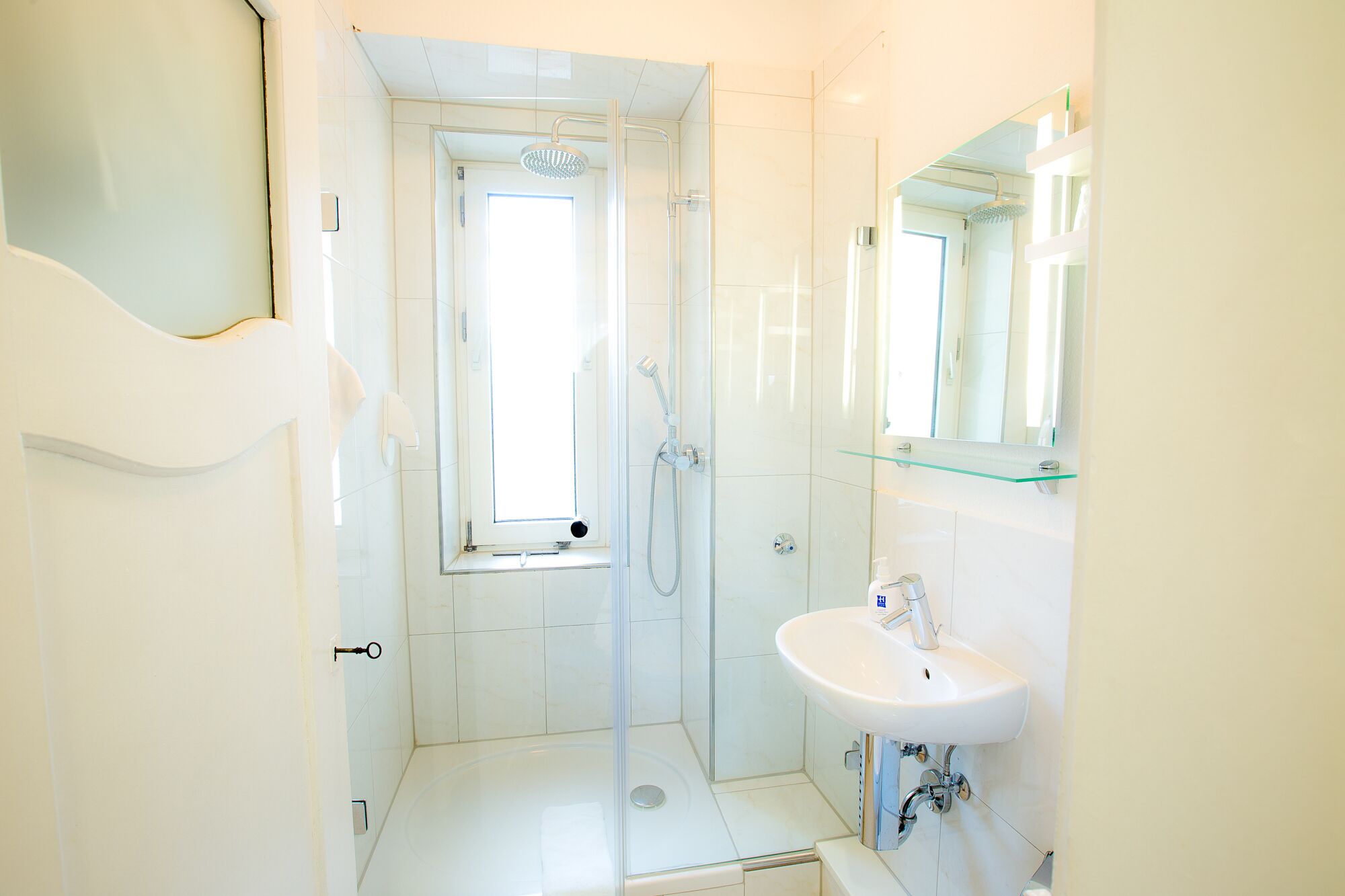 A modern bathroom with a glass shower enclosure, a white sink, and a glass shelf above the sink.