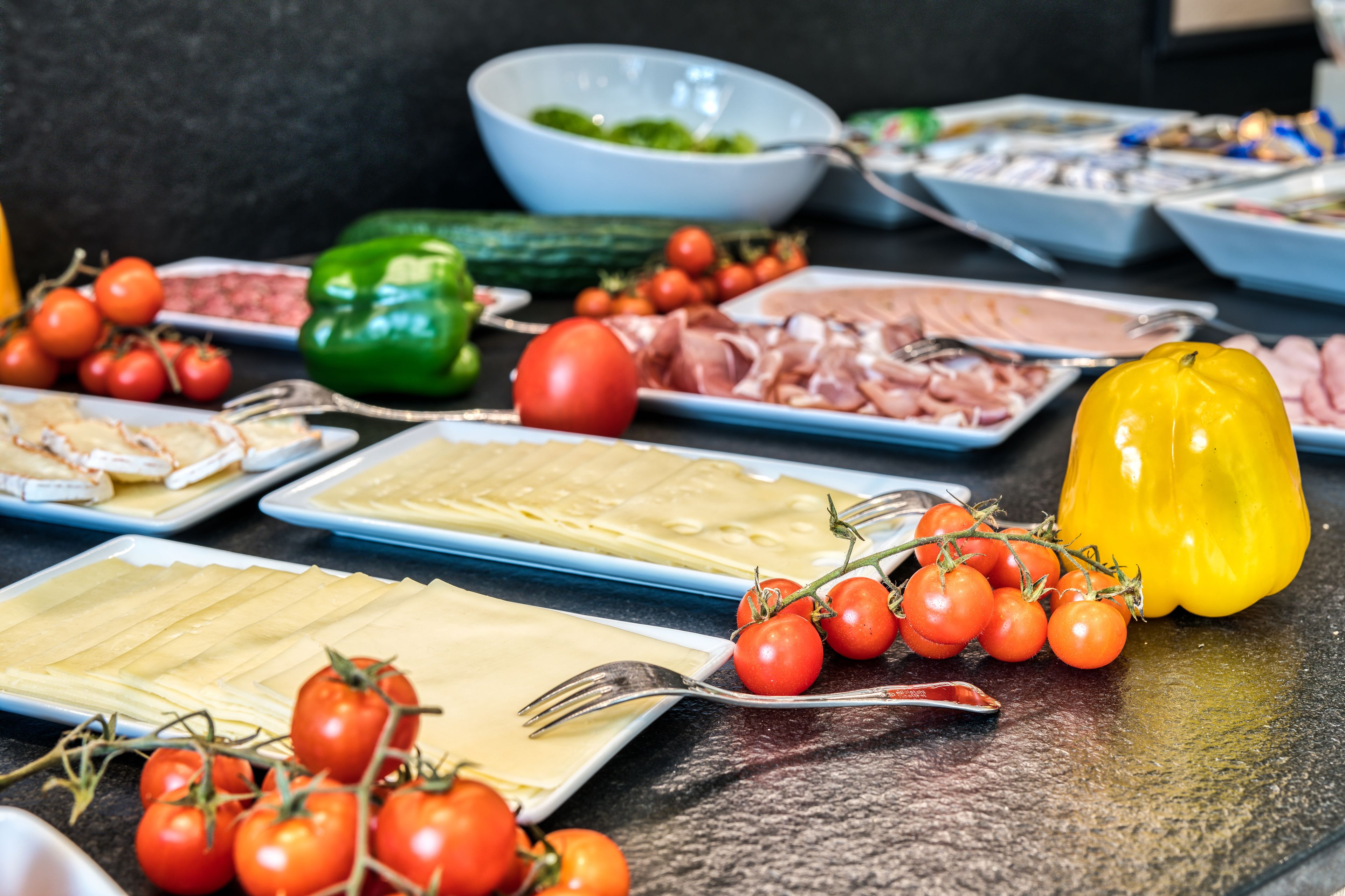 A buffet table with various food items including cheese, meats, and vegetables.