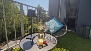 Ein runder Tisch mit einer Flasche, Gläsern und einem Stück Käse auf einem Balkon mit Blick auf Bäume.
