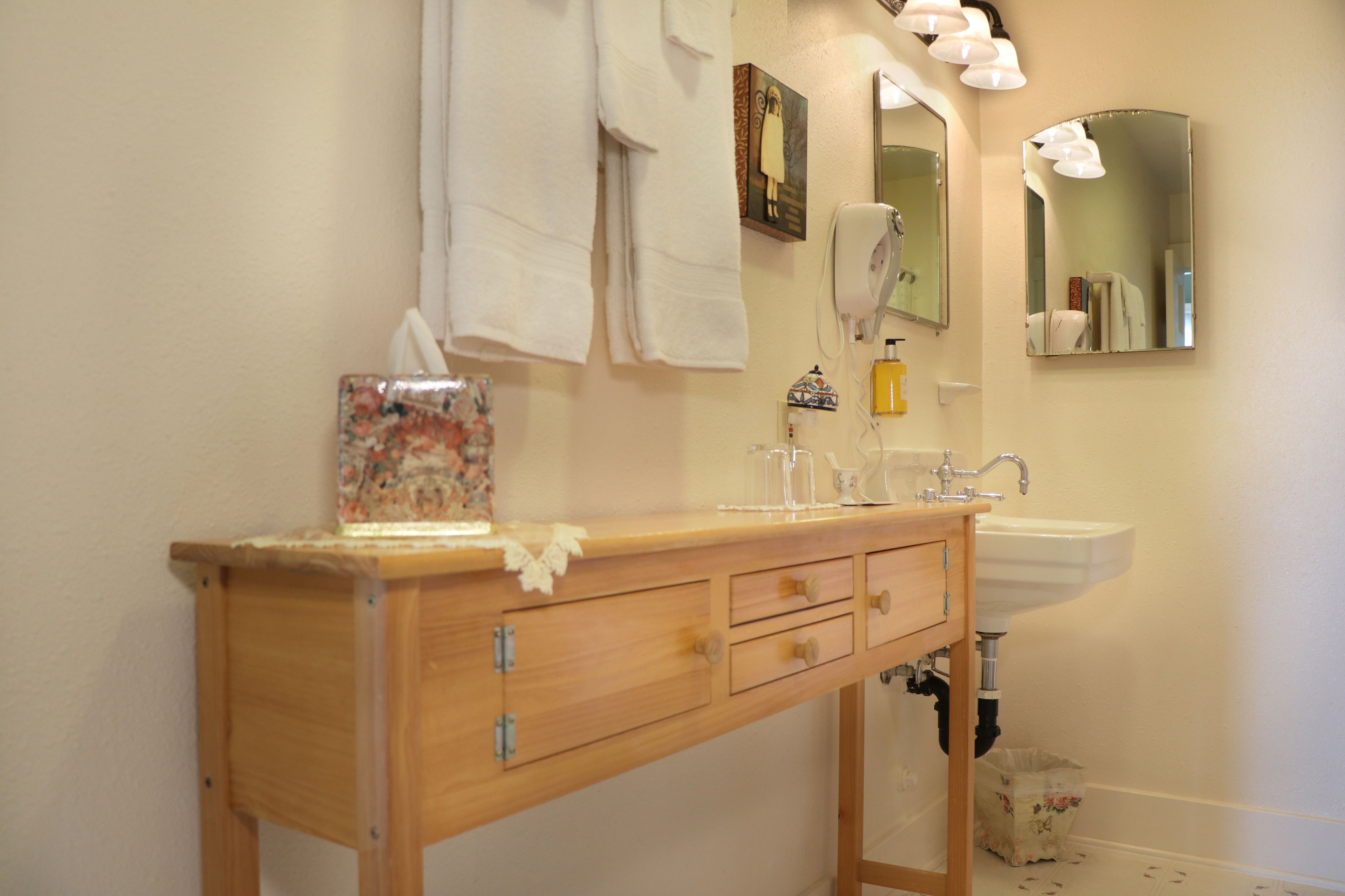 A wooden vanity with a sink and mirror, towels hanging above, and a tissue box on the counter.