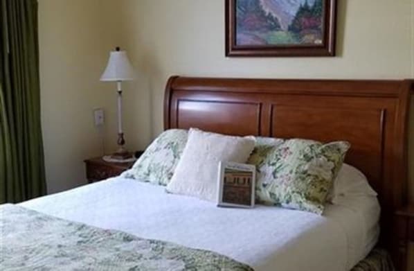 A neatly made bed with a floral bedspread, a framed painting above it, and a lamp on a bedside table.