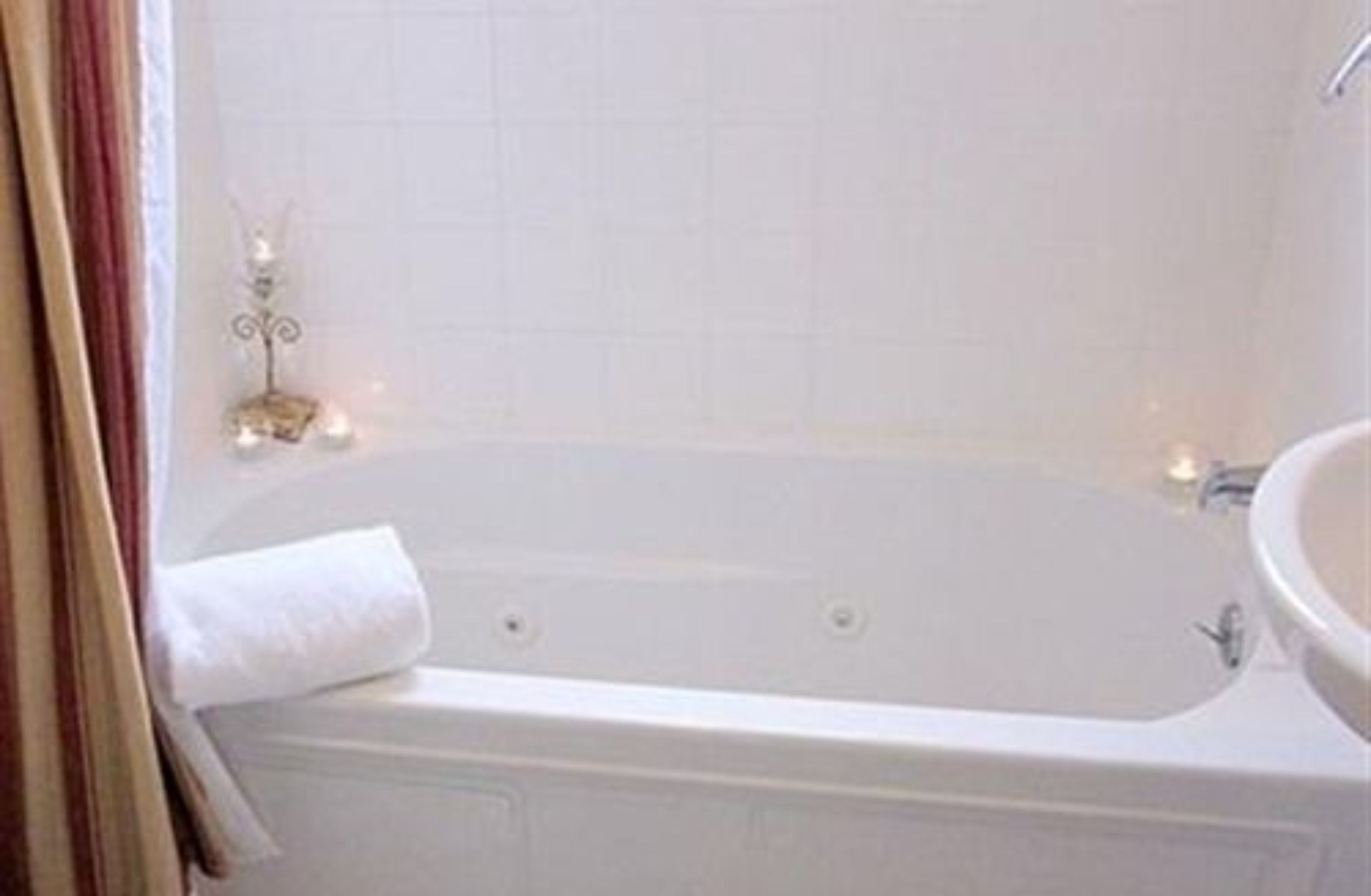 Uma banheira branca com um pequeno objeto decorativo ao lado, uma pia branca e uma cortina parcialmente visível.