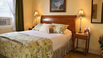 A neatly made bed with floral bedding, two bedside lamps, a nightstand with a lamp, a framed picture on the wall, and a window with curtains.