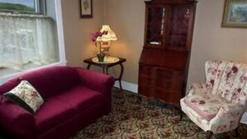 A room with a red sofa, a floral armchair, a wooden cabinet, and a patterned carpet.