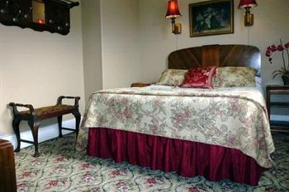 Un dormitorio con colcha estampada, cabecero de madera, dos lámparas de pared y una mesita de noche con lámpara.