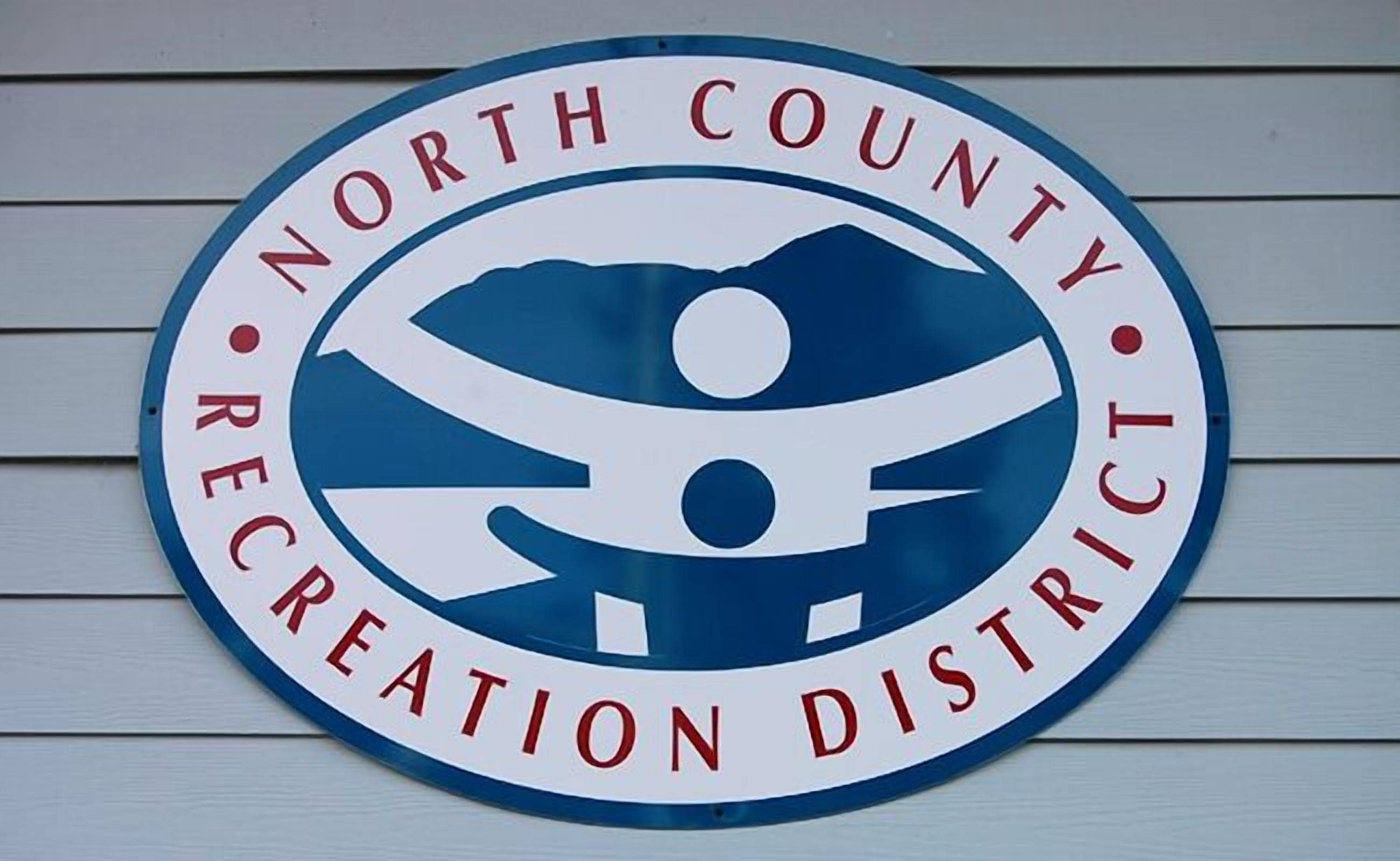 A circular sign with the text "North County Recreation District" and a graphic of a person holding a flag.