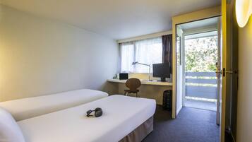 A hotel room with two single beds, a desk with a computer, a chair, and a view of the outdoors through a door.