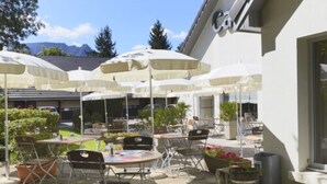 An outdoor patio with multiple tables and chairs, surrounded by umbrellas, and a building with a sign that reads "Cav."