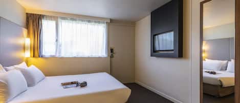 Habitación de hotel con cama, ventana con cortinas, televisor montado en la pared y un espejo.