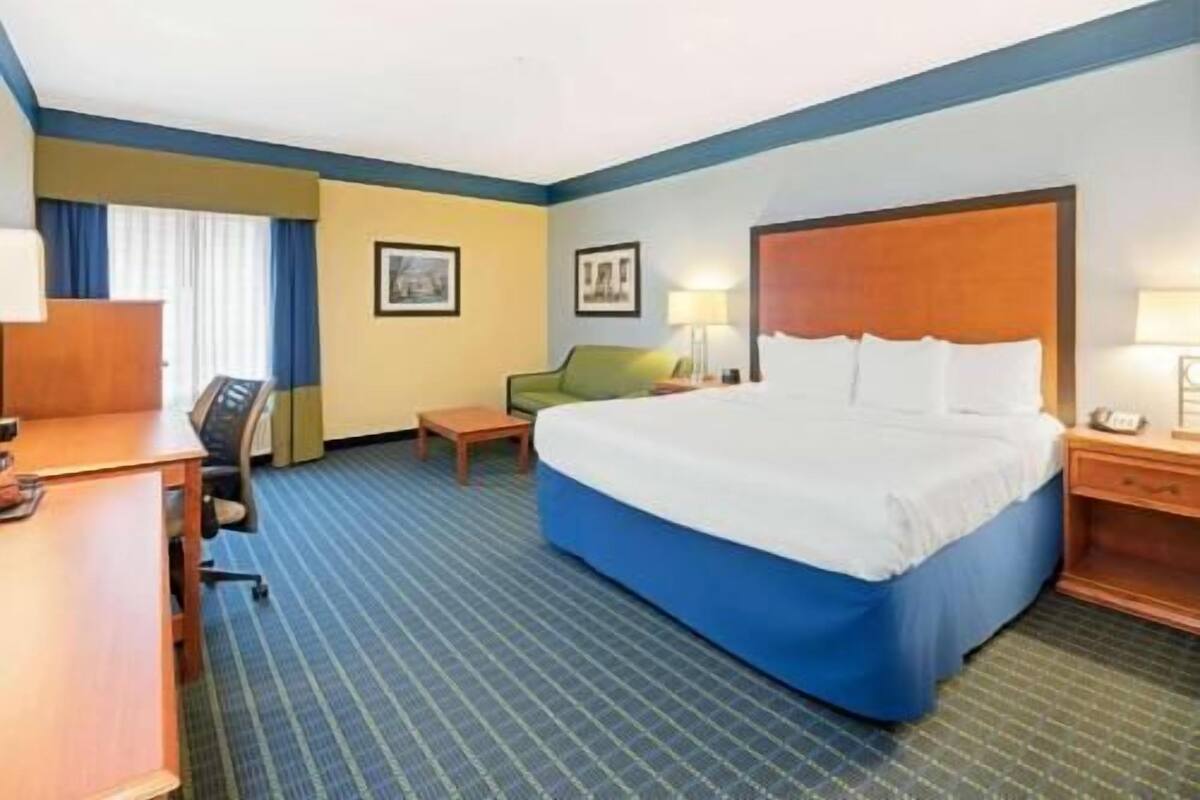 A hotel room with a large bed, a desk, a chair, and a small table.