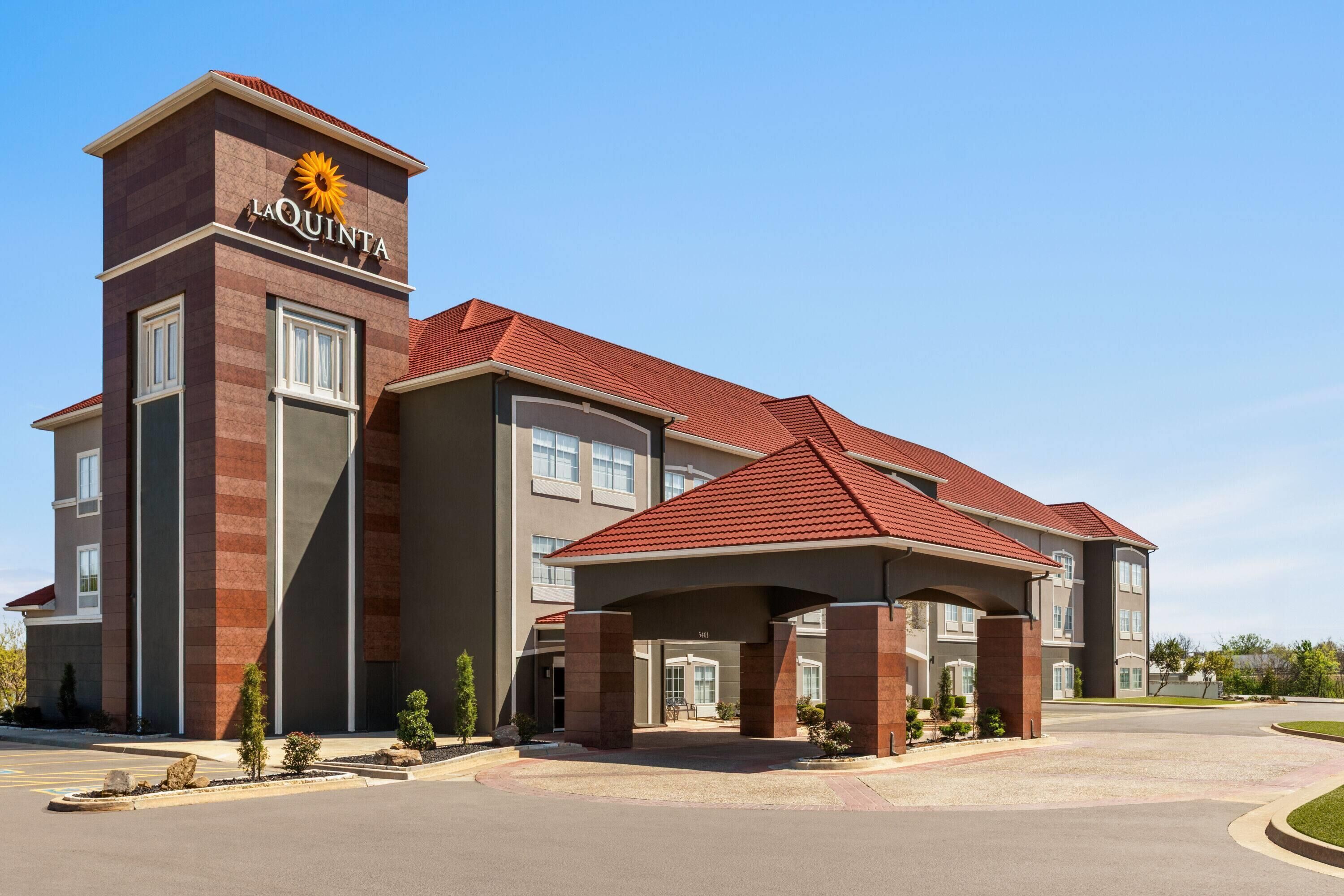 A hotel with a prominent tower featuring the name 'LAQUINTA'. It has a modern design with a red-tiled roof and a covered entrance area.