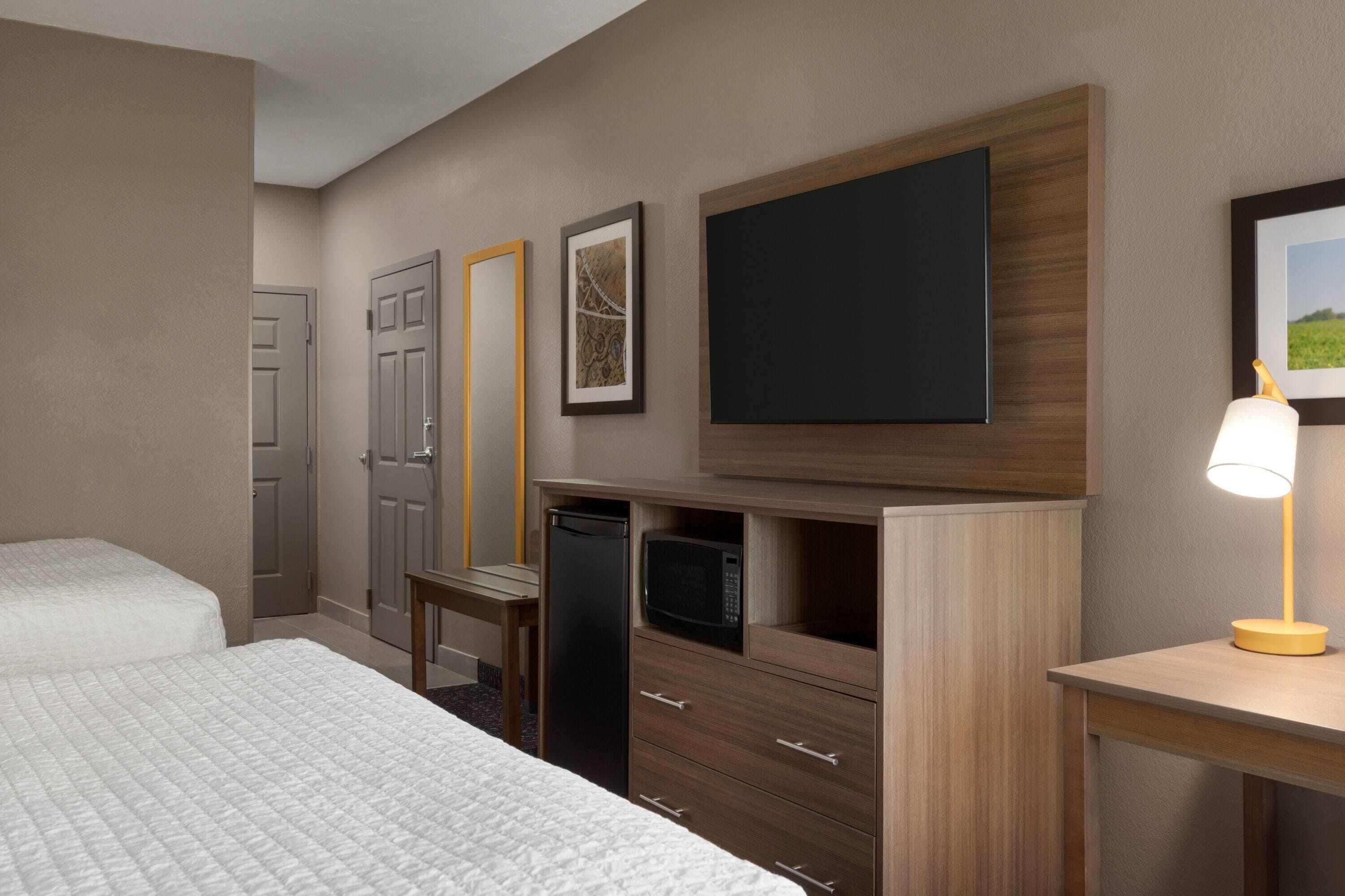 Een hotelkamer met twee bedden, een bureau met lamp, een magnetron en een televisie aan de muur.