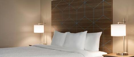 Une chambre d’hôtel avec un grand lit, deux tables de chevet avec des lampes et une tête de lit à motifs géométriques.