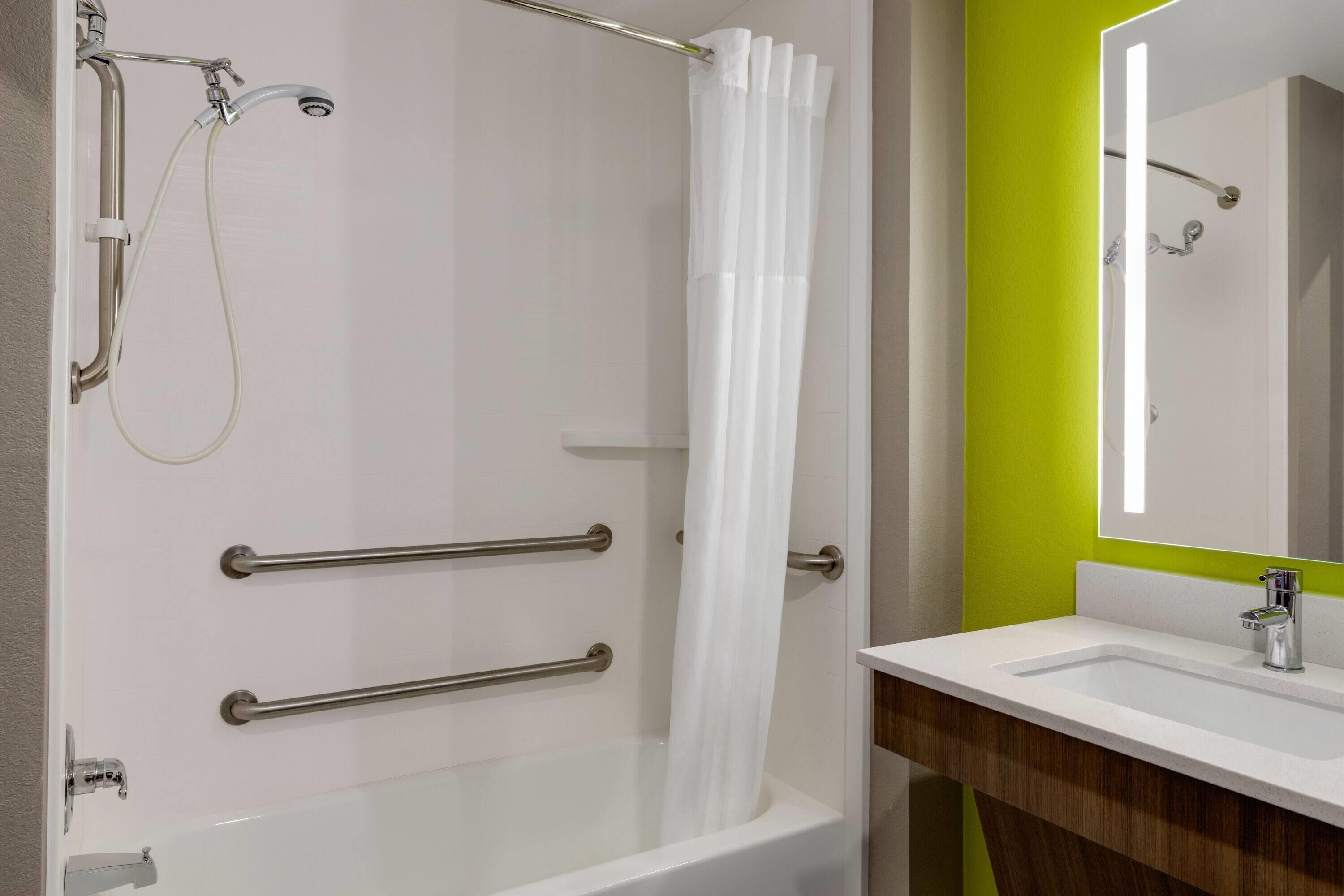 A bathroom with a white bathtub, a shower with a white curtain, and a sink with a mirror.