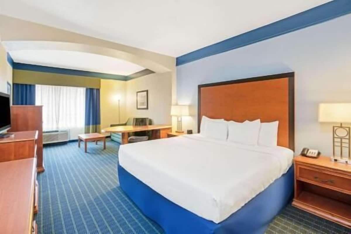 A hotel room with a large bed, a desk, a chair, a TV, and a window with curtains.