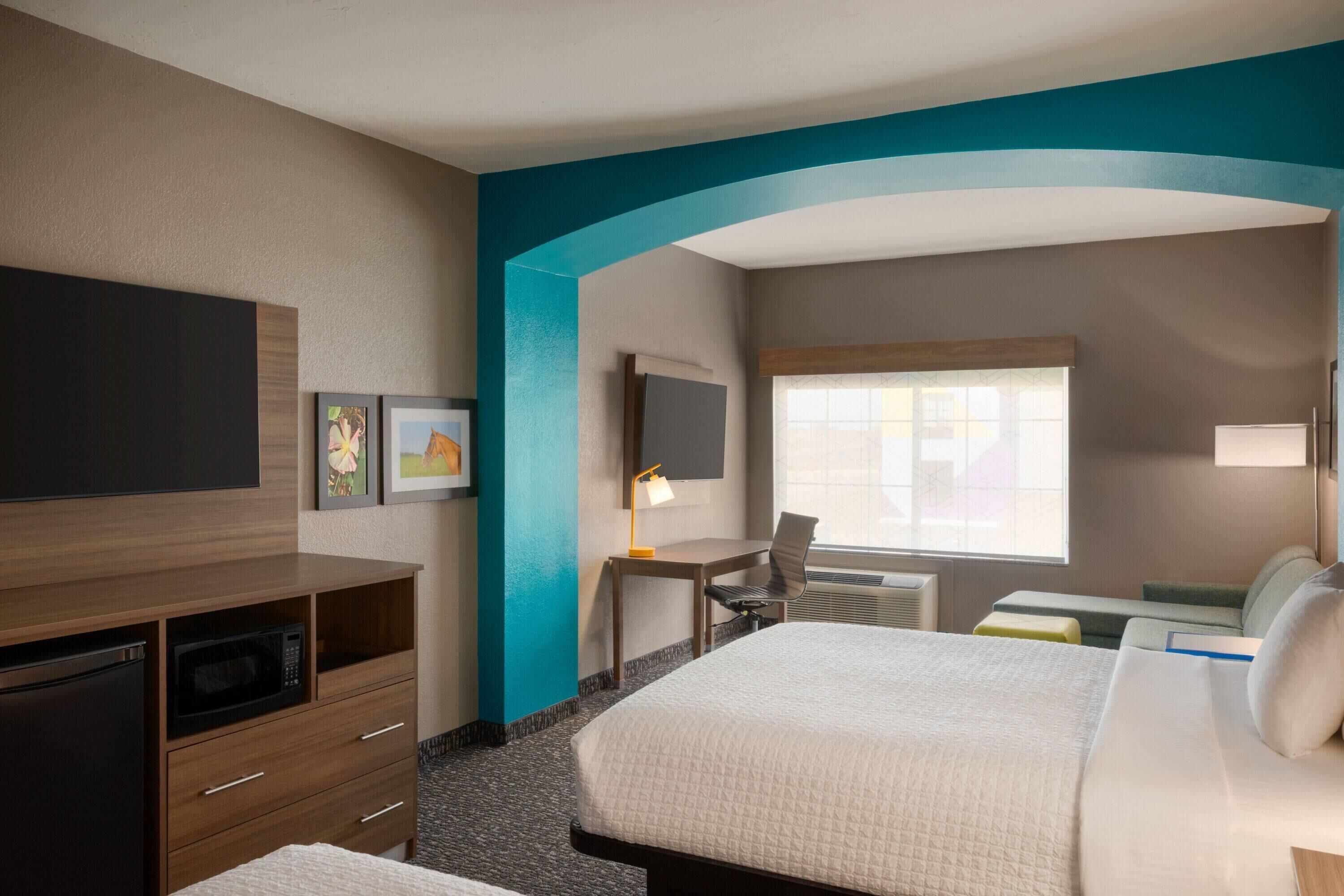 Una habitación de hotel con cama, escritorio, silla, televisor y microondas.